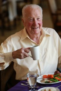 A senior man holding eating a gourmet breakfast, holding a cup of tea. Elderly man in retirement home Canada.