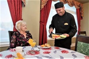 Senior lady sitting at a table being served breakfast by a waiter