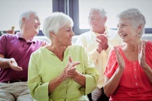 Senior women clapping and singing with men laughing in the background