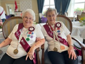 Two older women with grey hair wearing Seniors Games T-shirts sporting medals