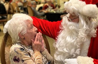 Santa Clause saying Merry Christmas to a surprised woman with short white hair