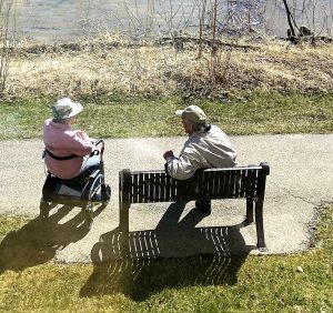 Older man sitting on a bench wearing a hat, talking to an elderly woman 