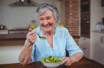 Woman with short grey hair wearing a blue shirt eating a salad.