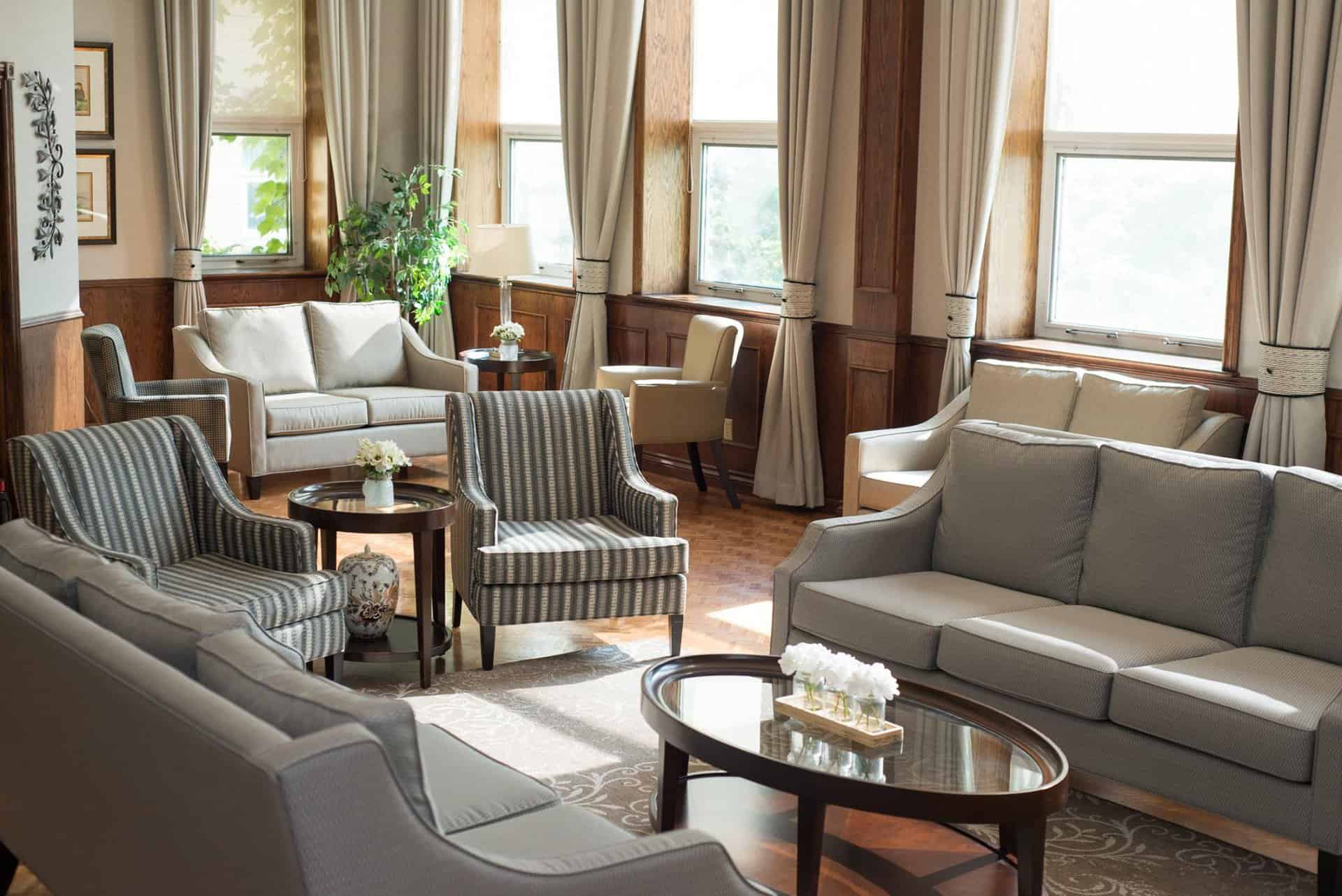 The Ultimate Guide To Moving into A Retirement Community (And A Checklist) - All Seniors Care Sun filled living area with grey couches and glass coffee table.