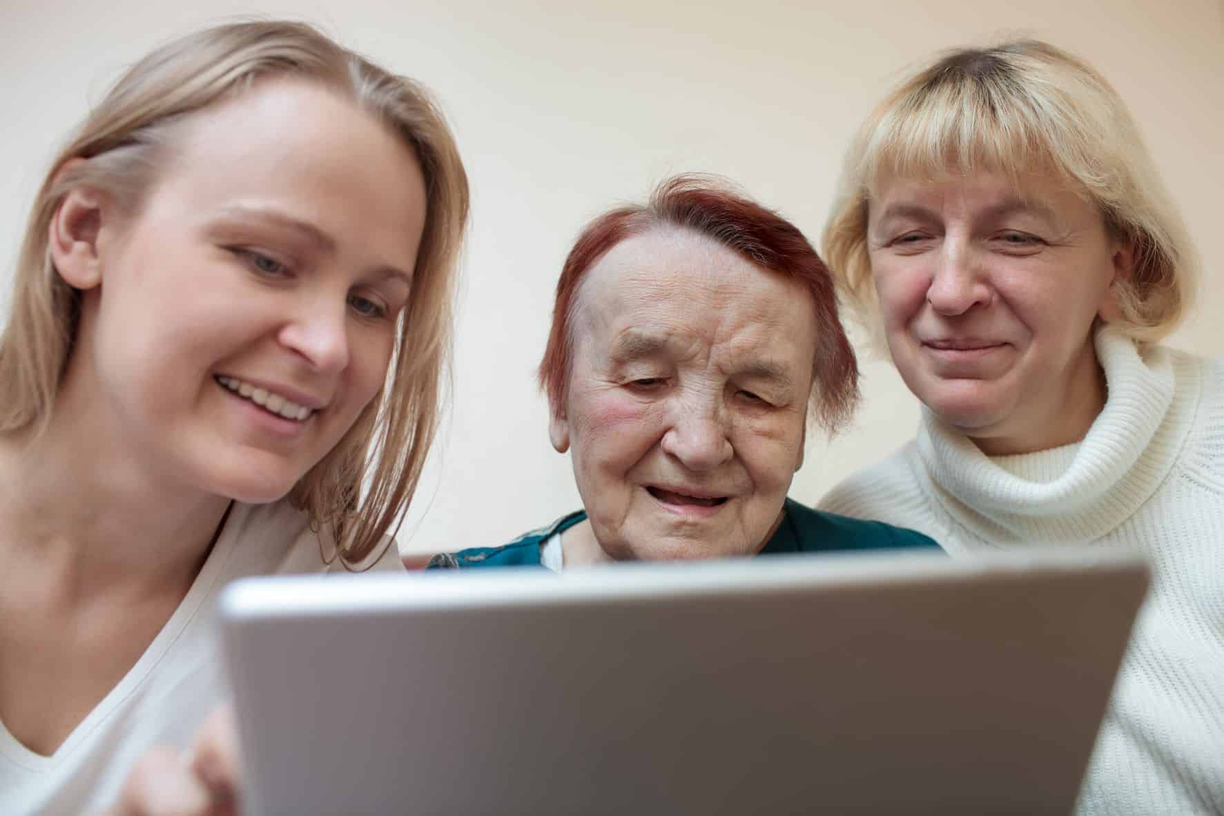Smiling senior, daughter, and granddaughter on a computer.