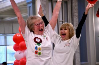 Senior with short hair and glasses celebrating a medal win with arms overhead cheering